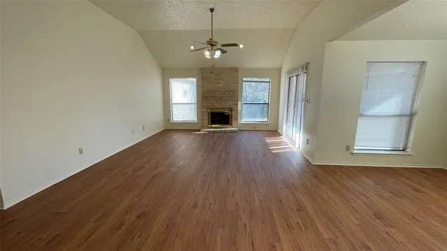 an empty room with wooden floor fireplace and windows