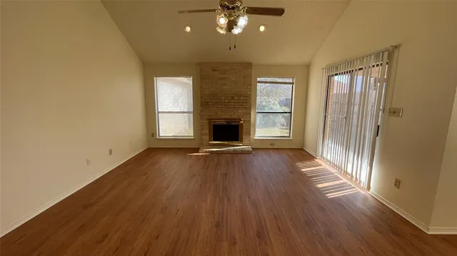 an empty room with wooden floor fireplace and windows