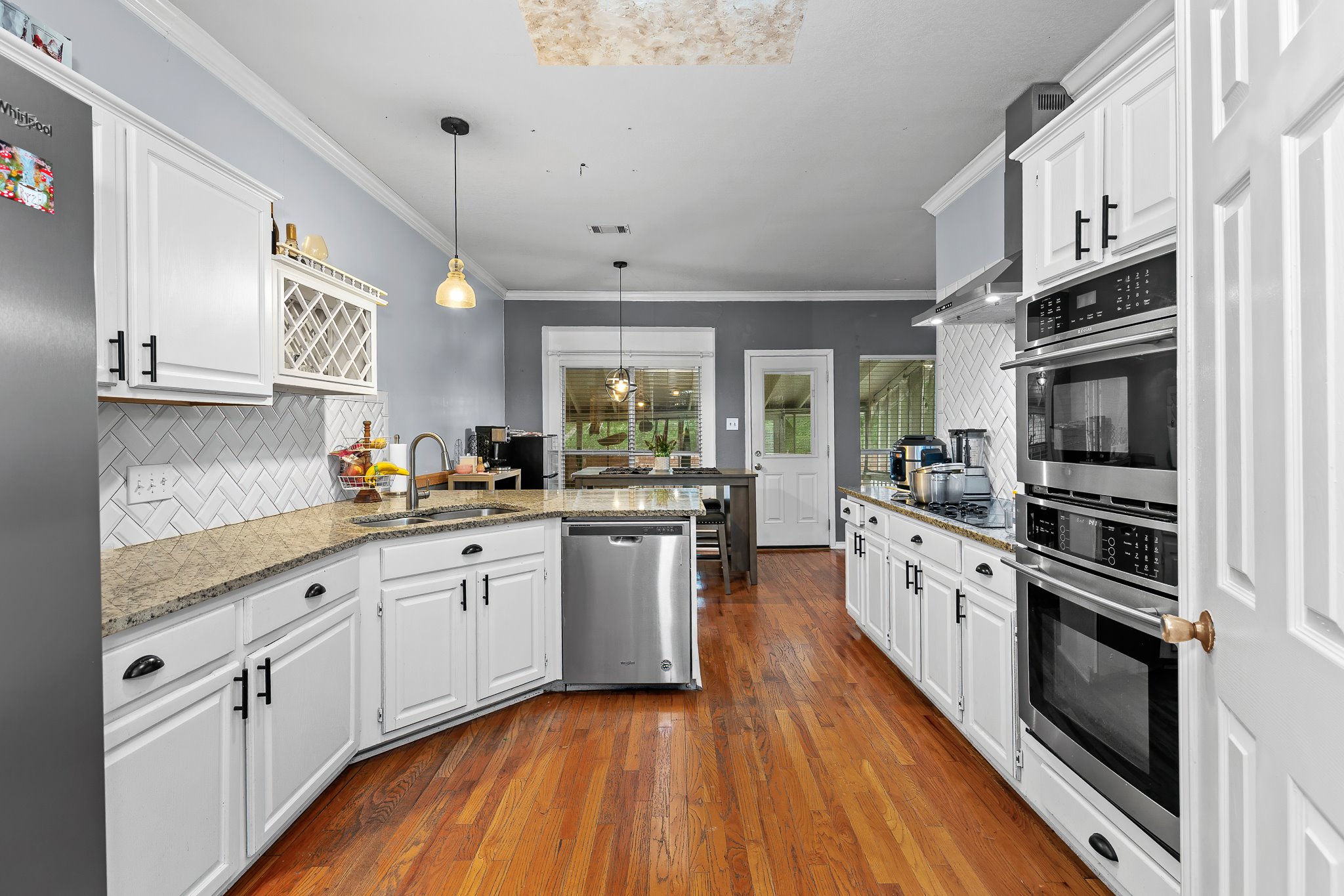 11737 Rydalwater Lane Austin, TX 78754 - Photo 23 of 40 Kitchen featuring white cabinetry with dark hardware, stone countertops, a white subway tile backsplash in a herringbone pattern, wood-finish flooring, and stainless steel appliances including a built-in double oven