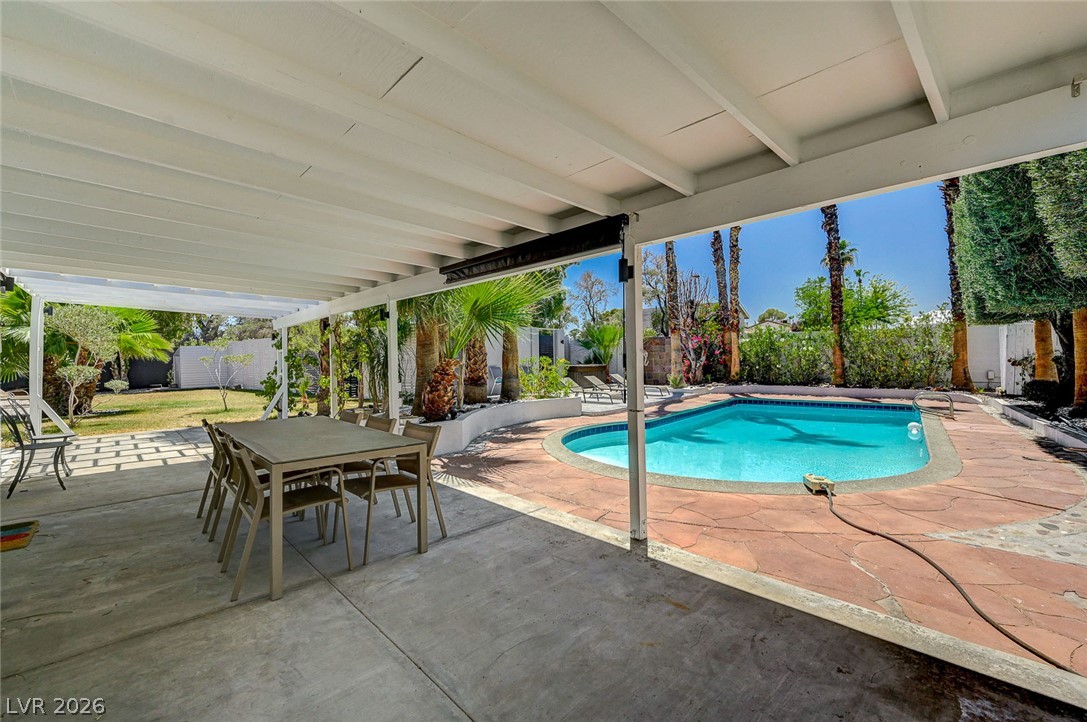 4153 Woodcrest Road Las Vegas, NV 89121 - Photo 43 of 58 A tranquil outdoor living space features a covered patio beside a refreshing pool, embraced by lush landscaping.