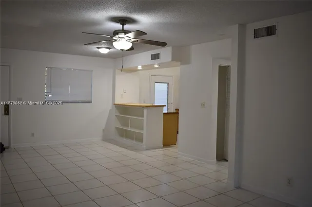 an empty room with kitchen and chandelier fan