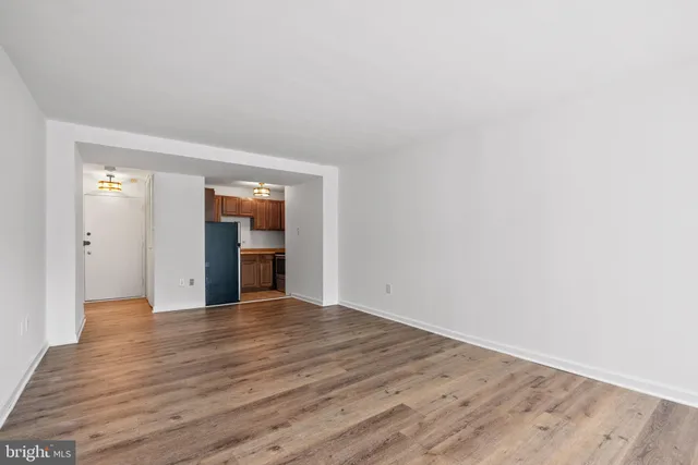 a view of an empty room with wooden floor and kitchen