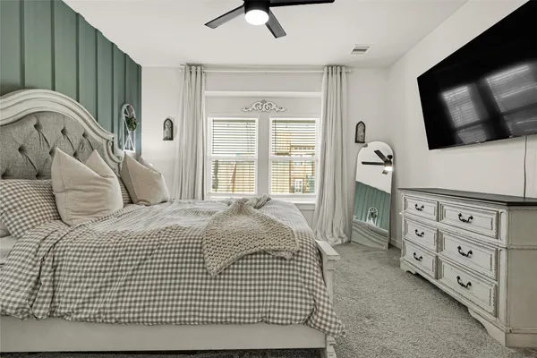 a bedroom with a bed next to a window with a flat tv screen on dresser