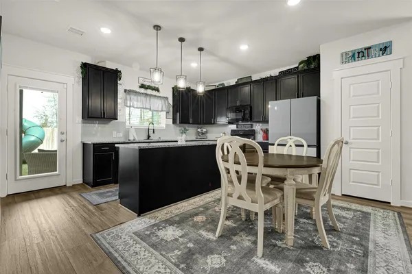a kitchen with stainless steel appliances kitchen island granite countertop a refrigerator a stove a sink a dining table and chairs with wooden floor