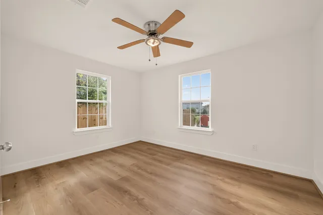 an empty room with wooden floor ceiling fan and windows