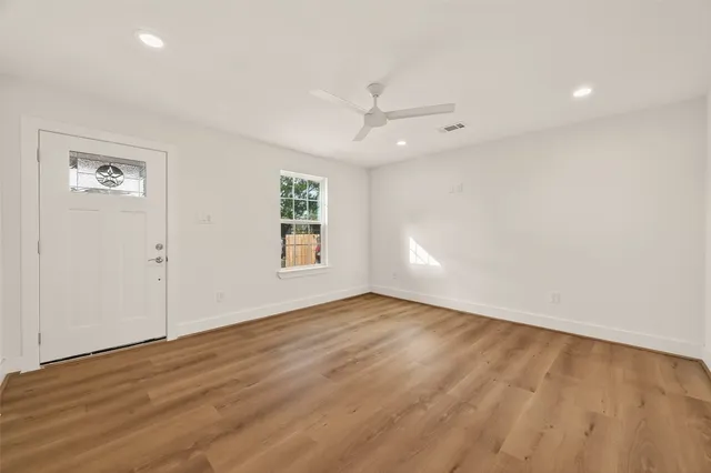 an empty room with wooden floor chandelier fan and windows