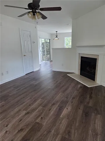 an empty room with wooden floor a ceiling fan a fireplace and windows