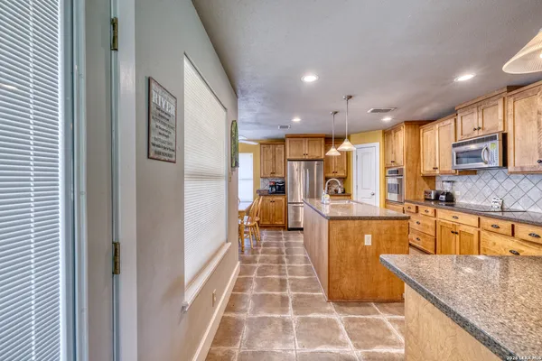 a view of a kitchen with granite countertop a dining table chairs stainless steel appliances and cabinets