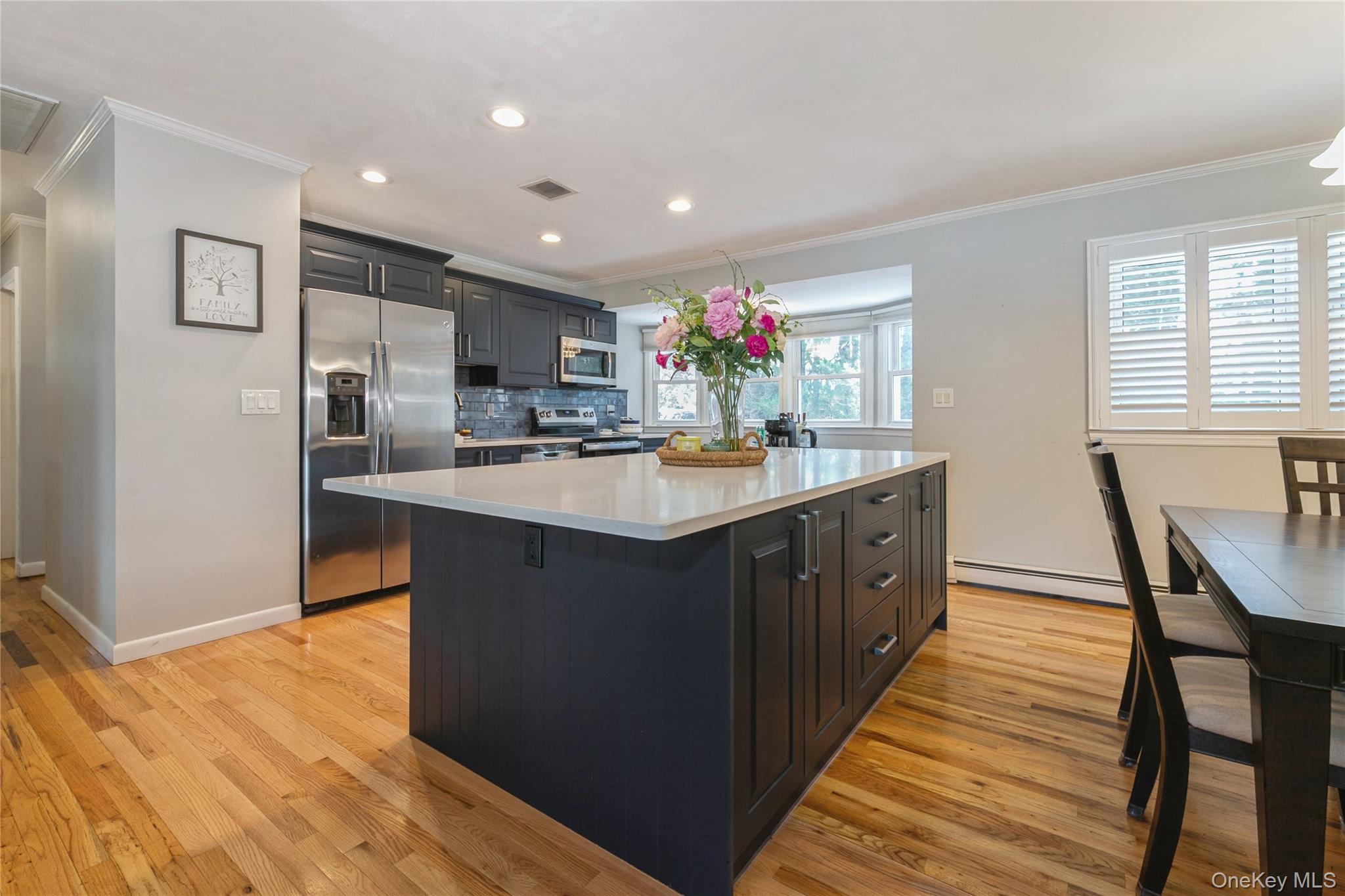 115 Clarendon Road Ronkonkoma, NY 11779 - Photo 10 of 45 Kitchen featuring a dark-toned island with storage, light countertop, stainless steel appliances, and wood-finish flooring