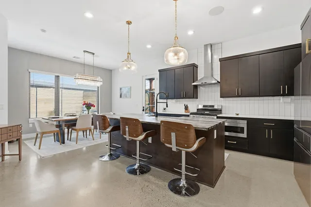 a open kitchen with stainless steel appliances granite countertop a stove a refrigerator a kitchen island a dining table and chairs with wooden floor