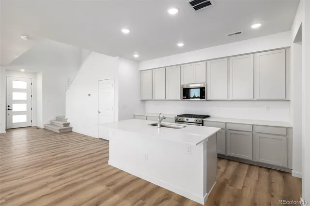 a kitchen with granite countertop a stove top oven a sink dishwasher and white cabinets with wooden floor