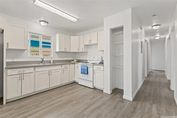 a kitchen with wooden floors white cabinets appliances and a window