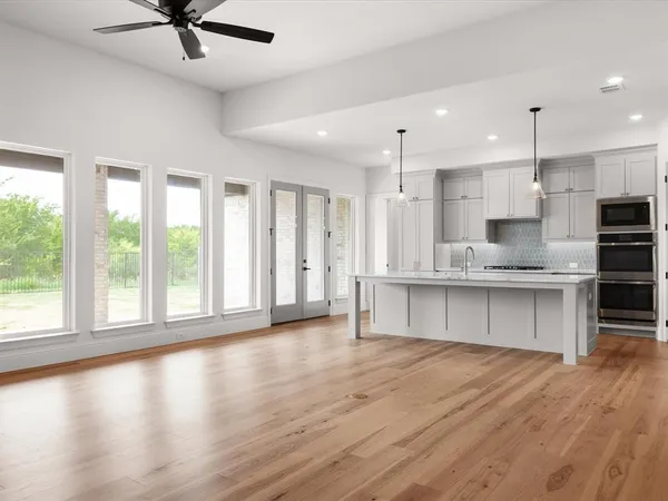 a large kitchen with stainless steel appliances granite countertop a stove a sink a refrigerator and white cabinets with wooden floor