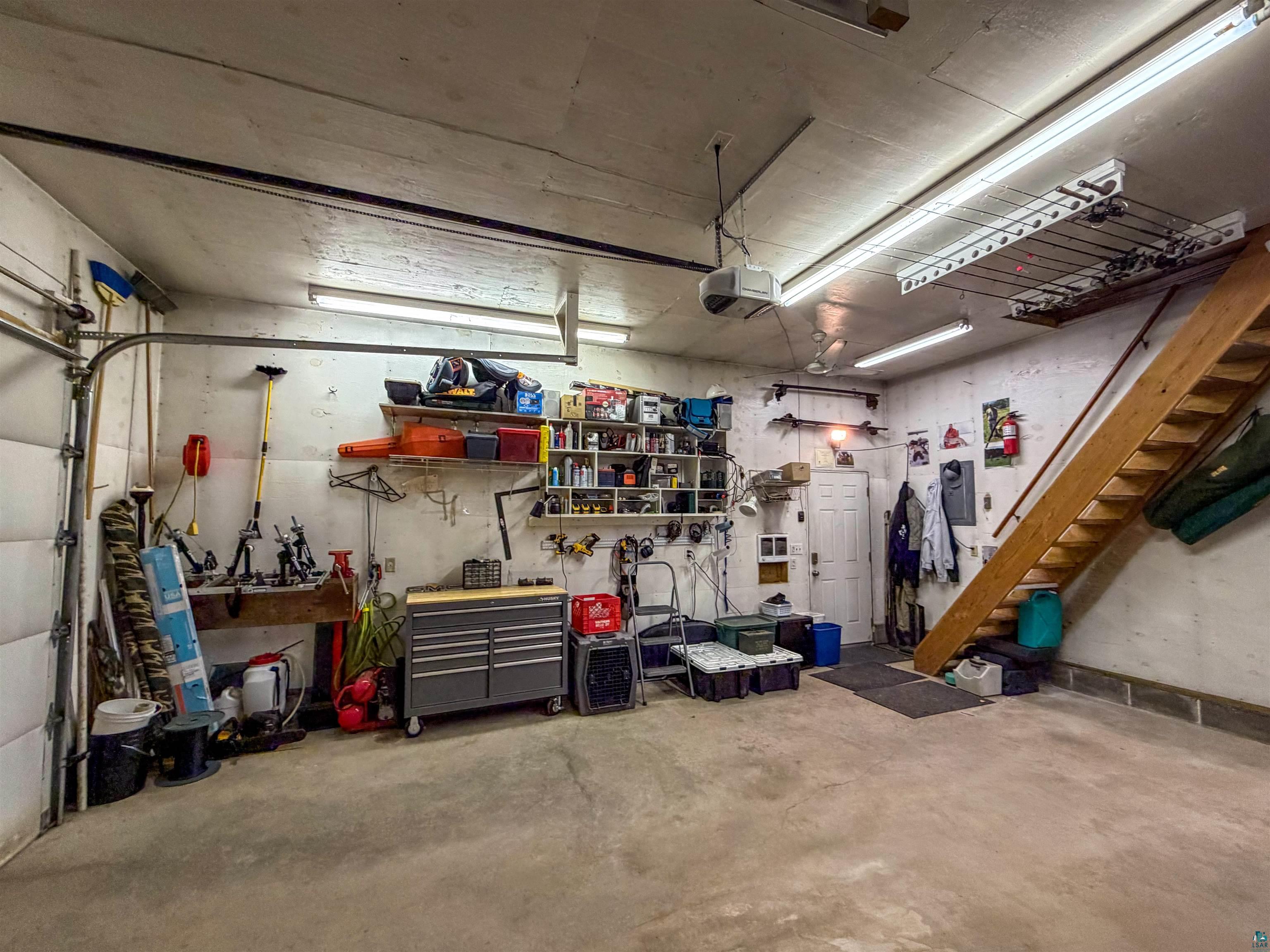 3704 Greysolon Road Duluth, MN 55804 - Photo 45 of 51 Spacious garage with concrete flooring, overhead lighting, an exposed wood staircase, built-in shelving, and a workshop area