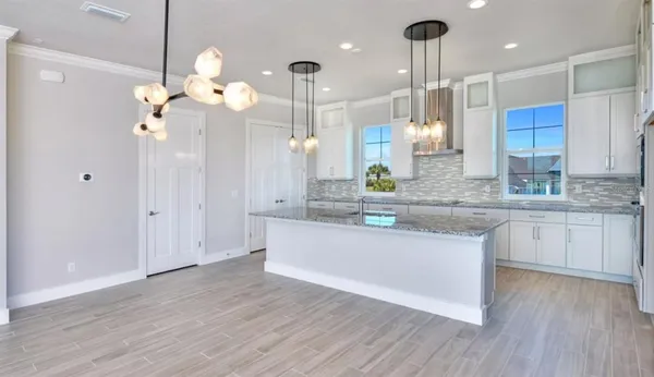 a large kitchen with granite countertop a white cabinets stainless steel appliances and a chandelier