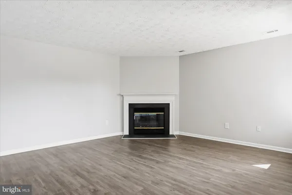a view of an empty room with wooden floor fireplace and a window
