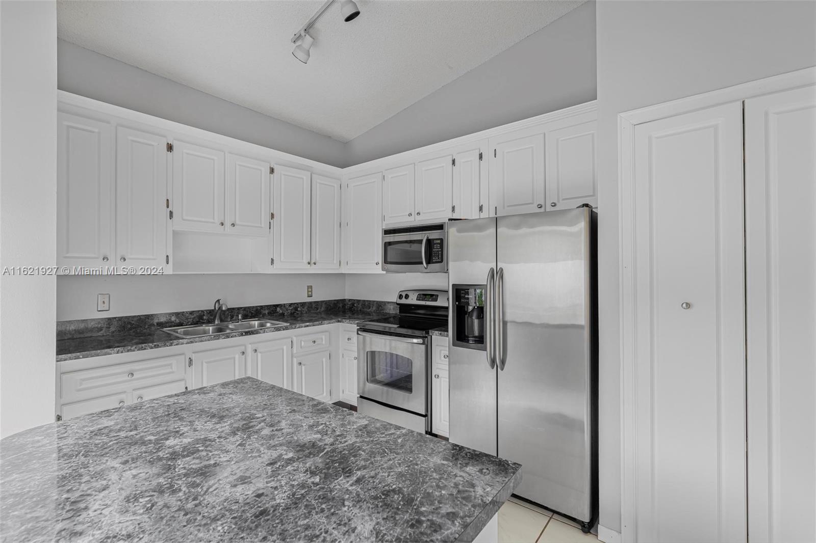 6604 Southwest 152nd Place, Unit 2604 Miami, FL 33193 - Photo 12 of 27 a kitchen with granite countertop a refrigerator stove and white cabinets