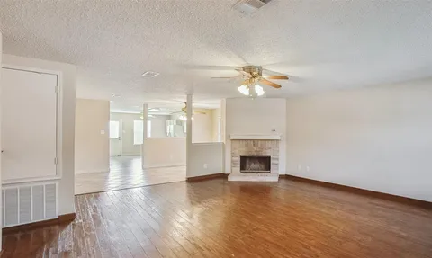 an empty room with wooden floor fireplace and windows