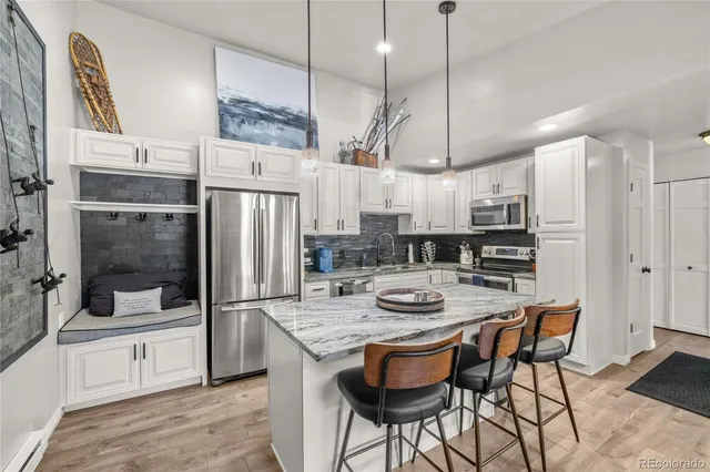 a kitchen with stainless steel appliances granite countertop a refrigerator a oven a sink a stove and a dining table with wooden floor