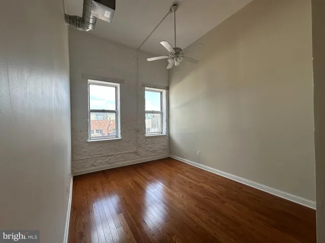 an empty room with wooden floor chandelier fan and windows