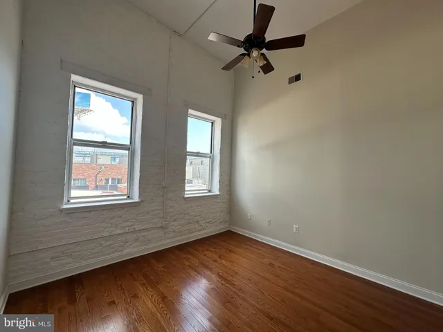 an empty room with wooden floor fan and windows