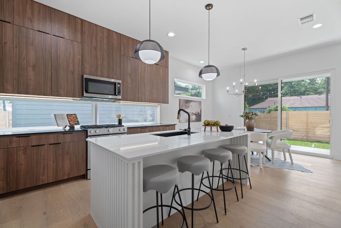 a kitchen with stainless steel appliances granite countertop a stove a sink a microwave a dining table and chairs with wooden floor