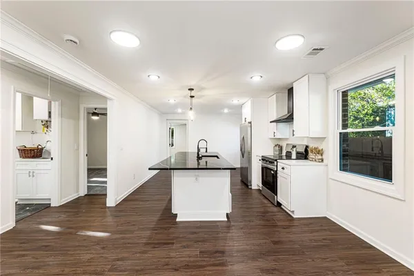a kitchen with stainless steel appliances granite countertop a stove top oven a sink dishwasher a refrigerator and white cabinets with wooden floor