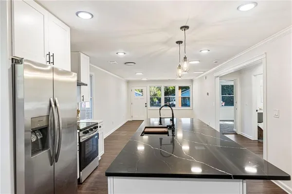 a view of a kitchen with stainless steel appliances granite countertop a sink a refrigerator and a view of living room