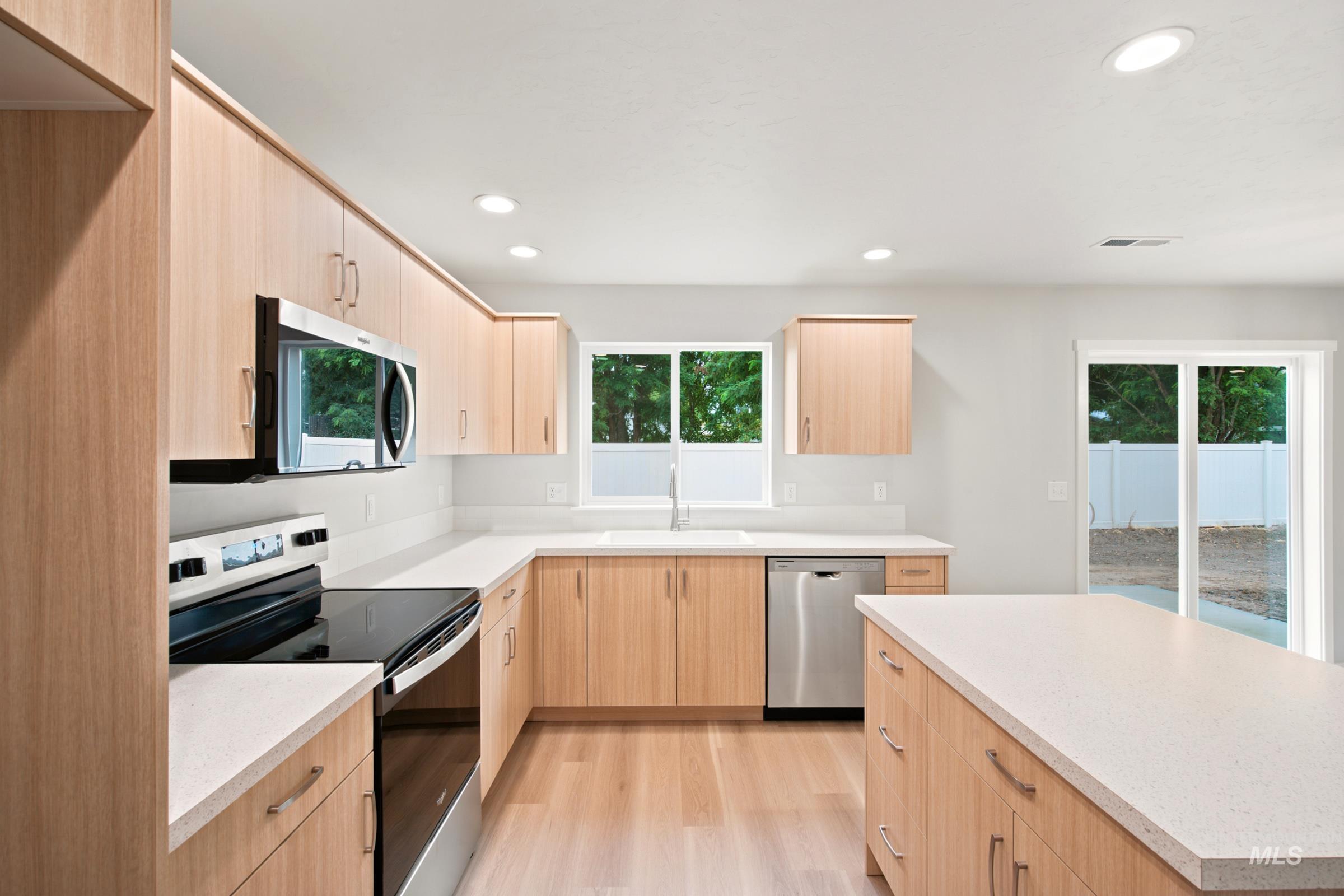 472 Merlin Court Middleton, ID 83644 - Photo 4 of 25 Open-concept kitchen featuring wood-finish cabinetry, light-toned countertops, stainless steel appliances, and wood-finish flooring
