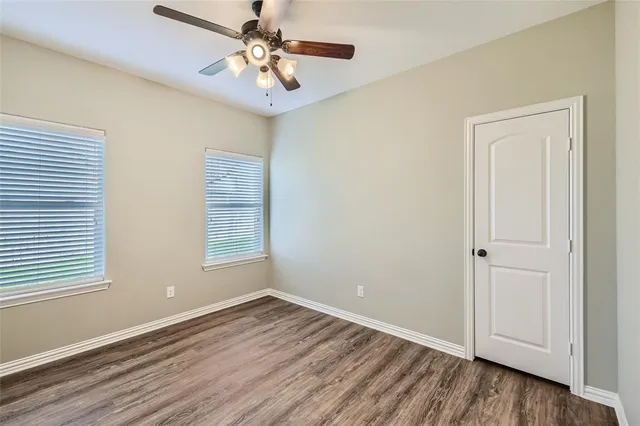 an empty room with wooden floor chandelier fan and windows