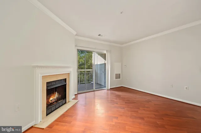 a view of an empty room with wooden floor fireplace and a window