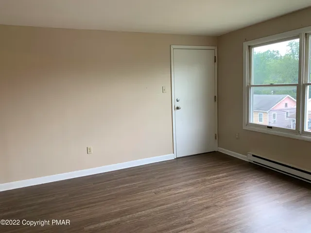 a view of an empty room with wooden floor and a window
