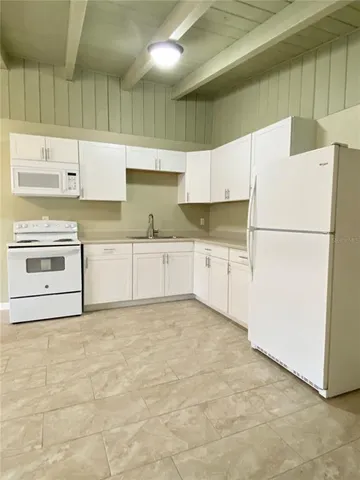 a kitchen with granite countertop a refrigerator a sink and white cabinets
