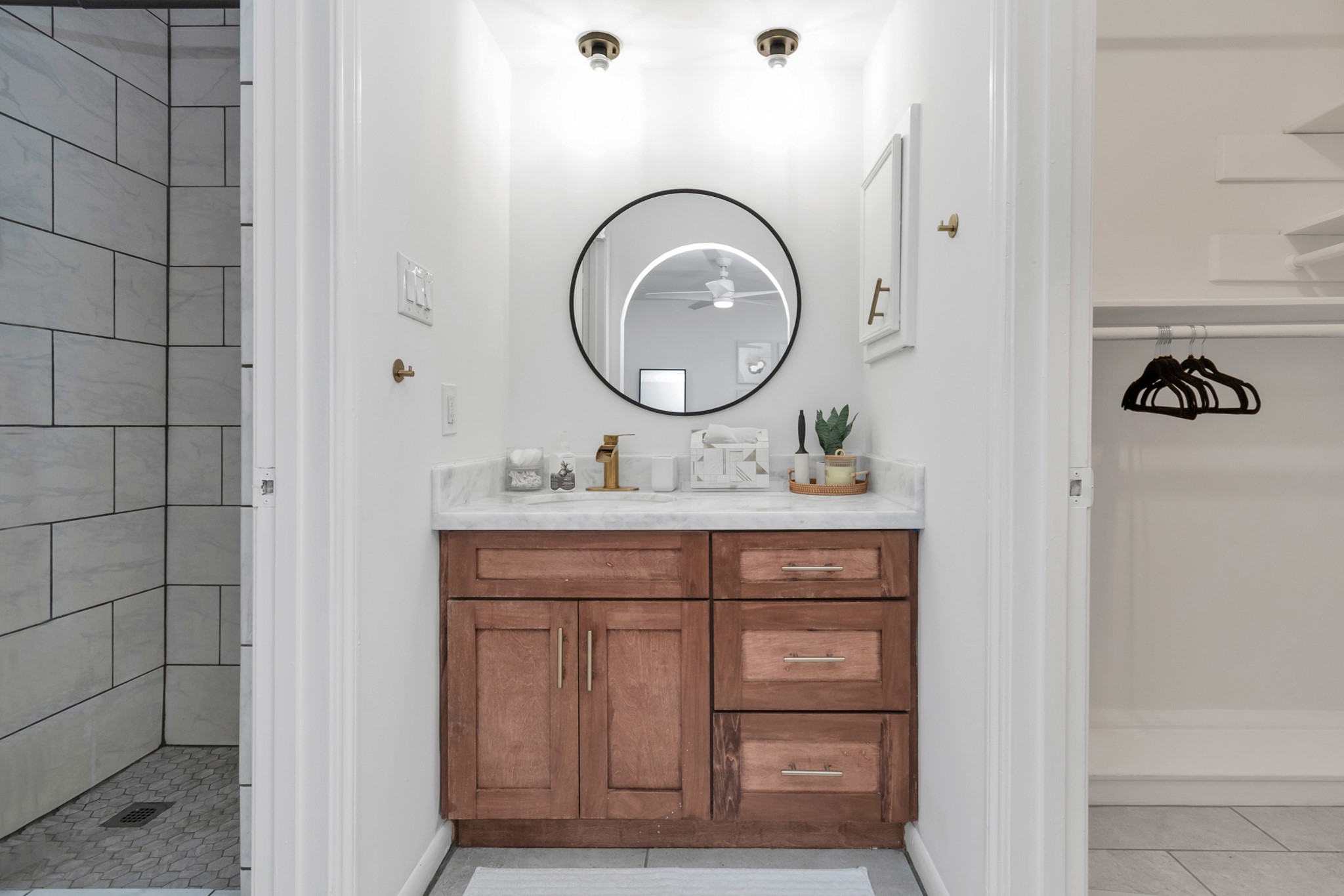 2718 Lazy Spring Drive Houston, TX 77080 - Photo 15 of 32 Updated bathroom with a modern vanity, round mirror, and stone countertop. Features wood cabinetry, a tiled shower, and an open closet with built-in shelving and hanging space. Clean and functional layout.