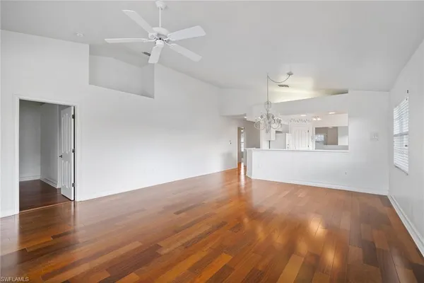 an empty room with wooden floor ceiling fan and windows