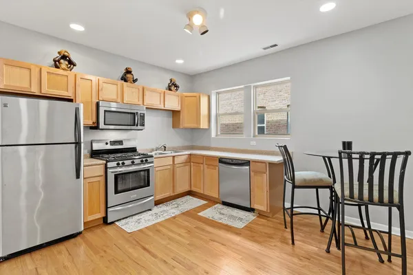 a kitchen with stainless steel appliances granite countertop a stove a sink a refrigerator a microwave a dining table and chairs with wooden floor