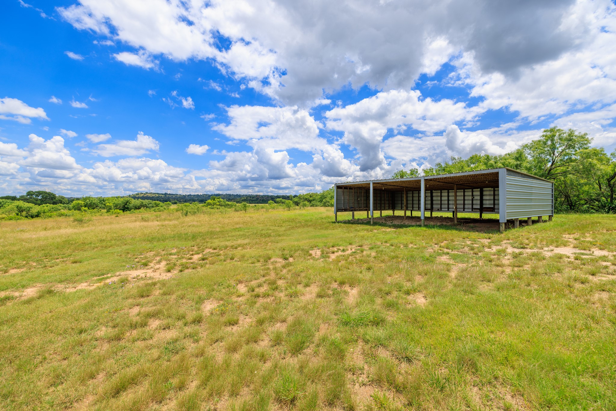 341 River View Road Fredericksburg, TX 78624 - Photo 32 of 40 An open-sided outbuilding sits on a vast grassy pasture under a dramatic cloud-filled sky.