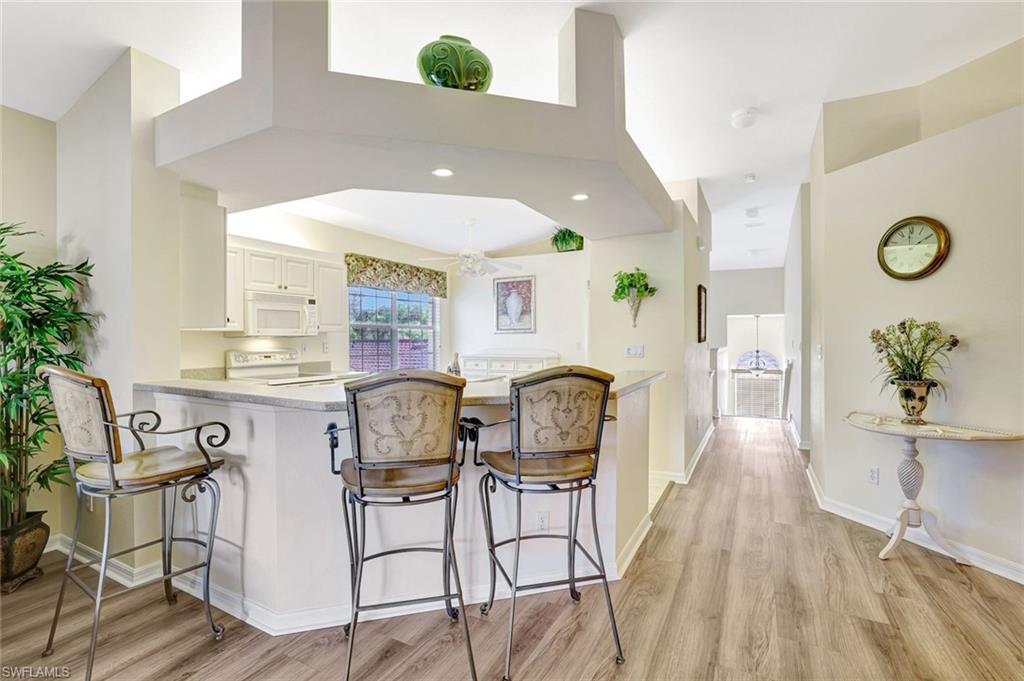 10910 Santa Margherita Road, Unit 204 Estero, FL 34135 - Photo 7 of 42 Kitchen featuring a breakfast bar area, white cabinets, white appliances, light wood-style flooring, and a peninsula