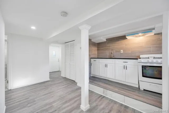 a open kitchen with granite countertop a stove top oven a sink and white cabinets with wooden floor