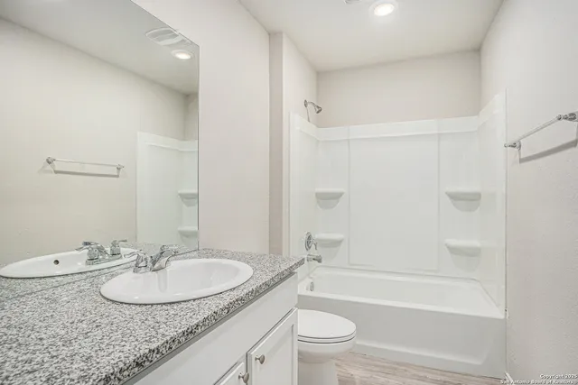 a bathroom with a granite countertop sink a toilet a mirror a bathtub and shower