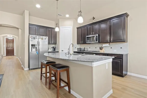 a kitchen with kitchen island granite countertop wooden cabinets a refrigerator a stove a microwave oven a refrigerator with island and chairs