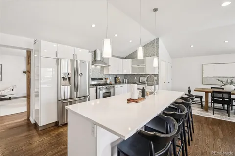 a kitchen with stainless steel appliances kitchen island a refrigerator a stove a sink and a dining table with wooden floor