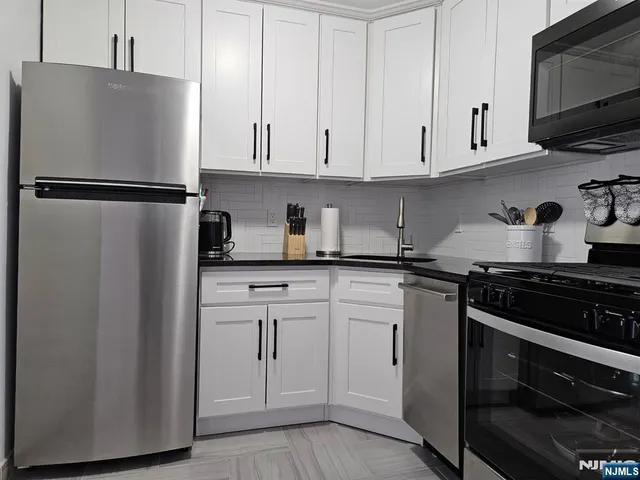 a kitchen with stainless steel appliances granite countertop white cabinets sink and a refrigerator