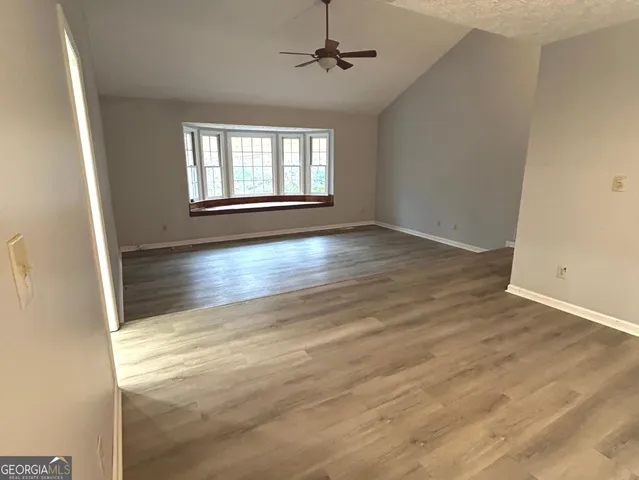 an empty room with wooden floor ceiling fan and windows