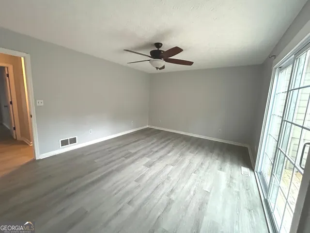 an empty room with wooden floor fan and windows