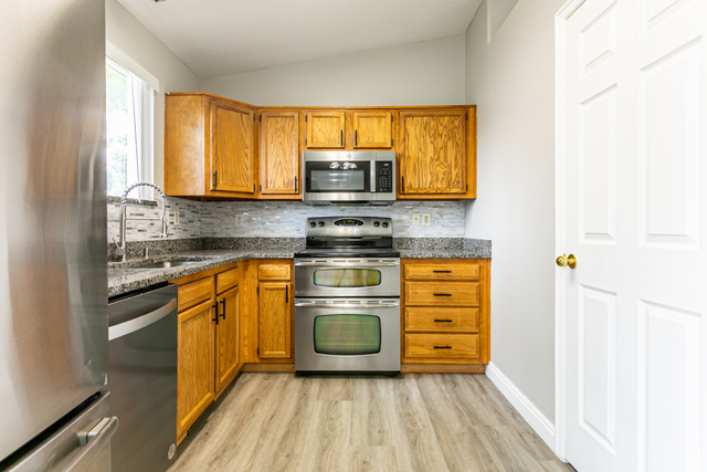 4239 West 5325th Street South Roy, UT 84067 - Photo 8 of 26 Kitchen featuring wood cabinetry, stainless steel appliances, granite countertops, a tiled backsplash, and wood-finish flooring