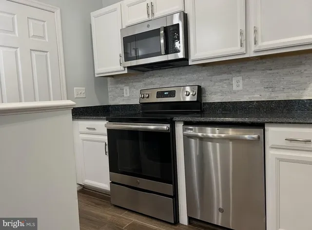 a kitchen with stainless steel appliances granite countertop white cabinets and a stove top oven