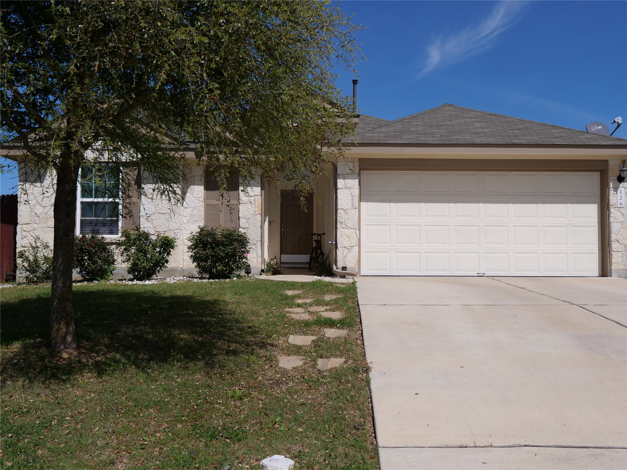 View of front of home with concrete driveway, roof with shingles, a front lawn, stone siding, and a garage