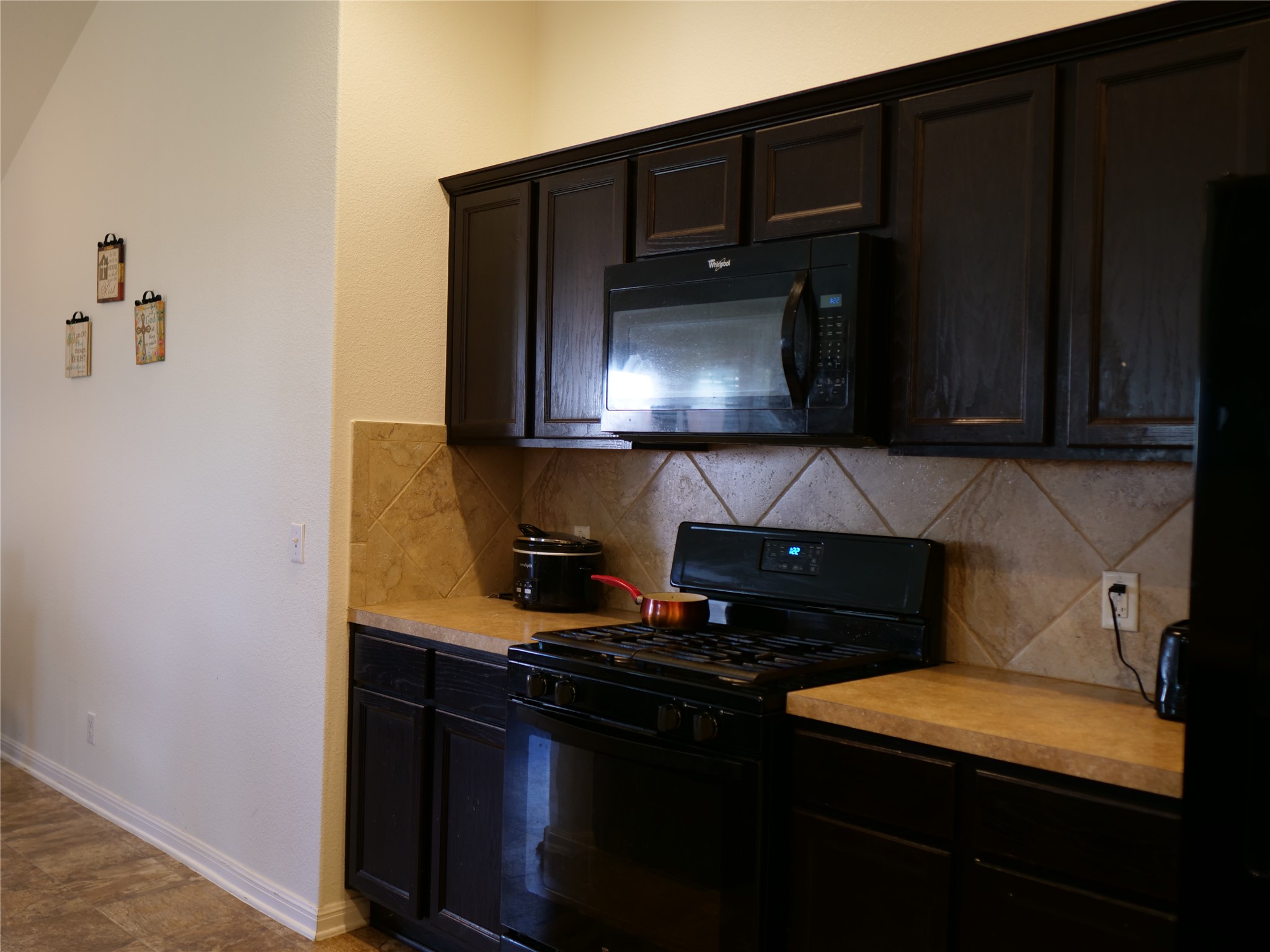 Undisclosed Address Elgin, TX 78621 - Photo 11 of 19 Kitchen with black appliances, light countertops, decorative backsplash, and dark wood finish cabinets