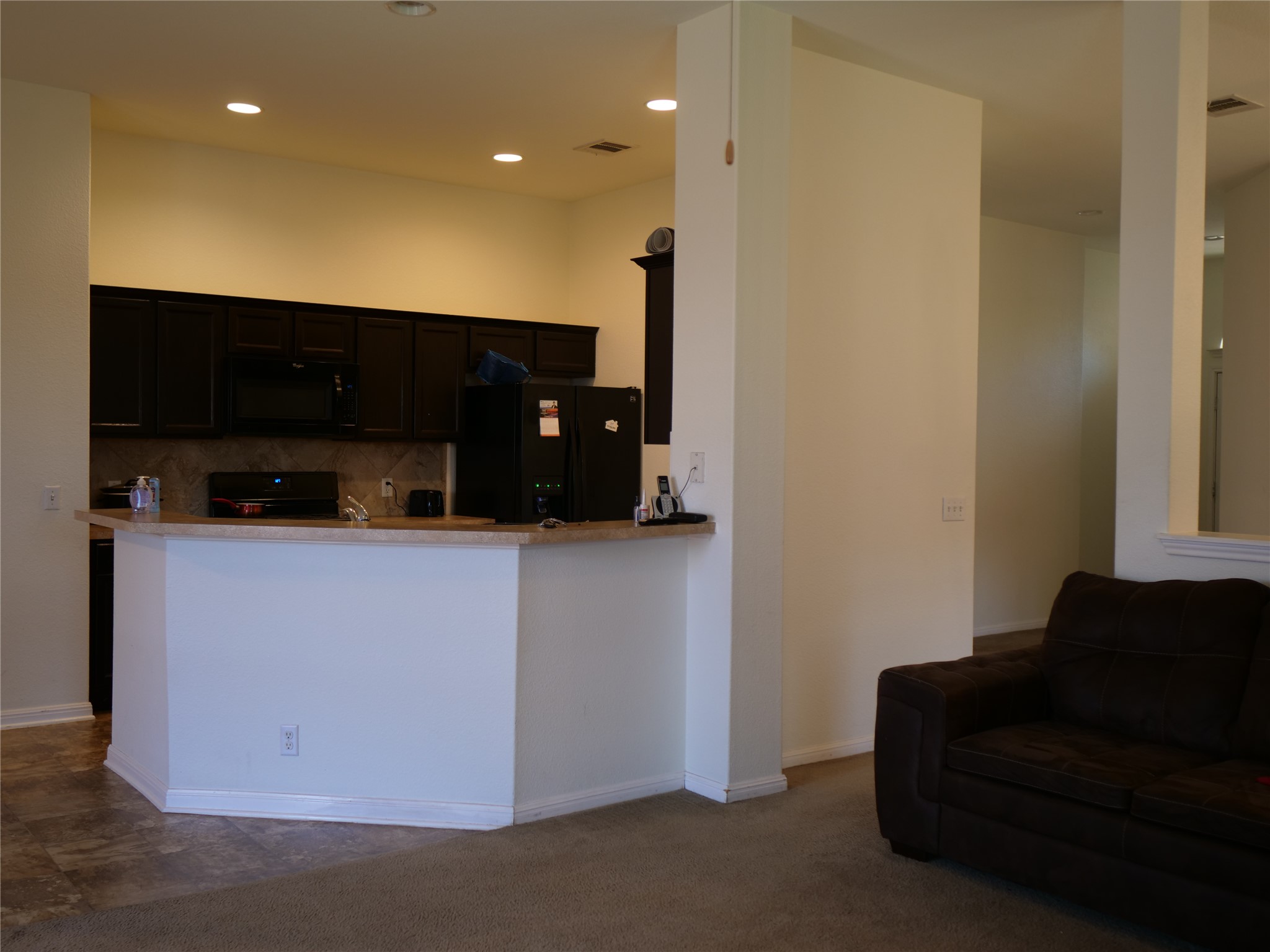 Undisclosed Address Elgin, TX 78621 - Photo 8 of 19 Kitchen featuring black appliances, dark cabinetry, backsplash, dark colored carpet, and light countertops